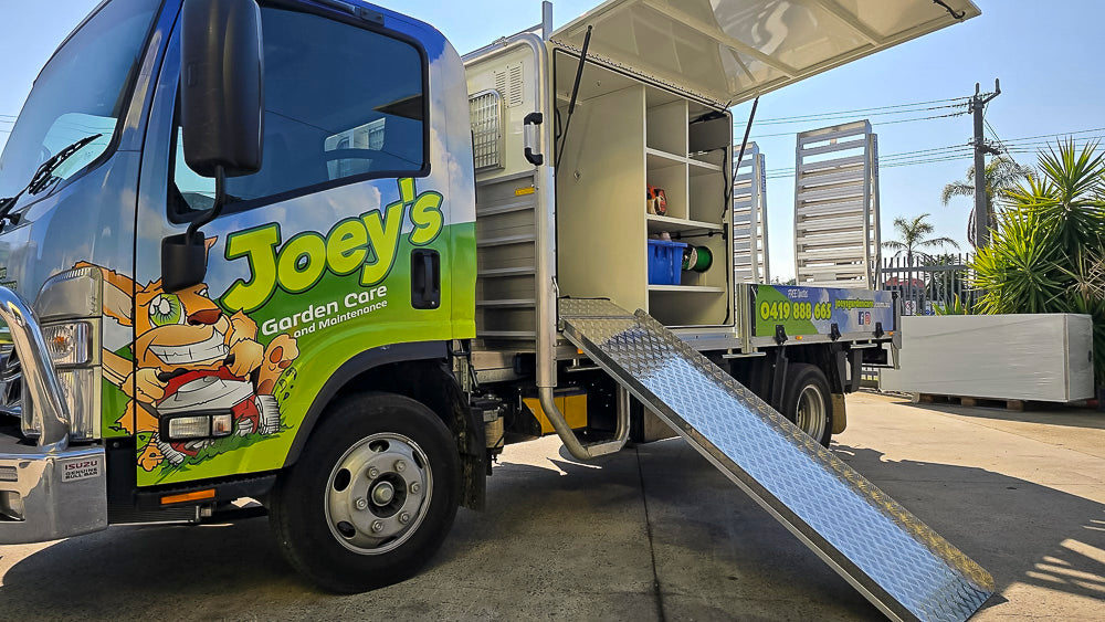 Custom mower truck service body with tool storage, gas-strut-assisted aluminium ramps, central locking, lighting and door safety buzzers, built by Metro Truck Body Builders Melbourne.