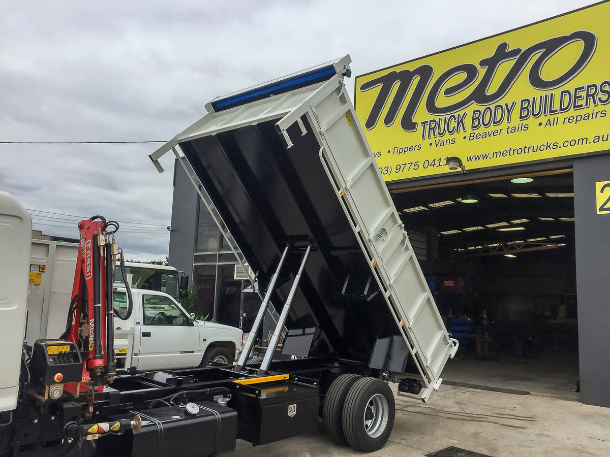 Custom split drop side tipper body with Fassi crane, retractable mesh tarp and toolbox built by Metro Truck Body Builders in Melbourne.